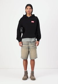 Sort hættetrøje med rød "DIESEL" logo, lagd oven på en grå skjorte. Båret med beige denim shorts og brune ankelstøvler. Sort telefonpouch på hættetrøjen.