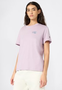 Lilac cotton t-shirt with short sleeves, featuring a small logo graphic on the chest and a logo patch on the sleeve. Simple, relaxed fit.