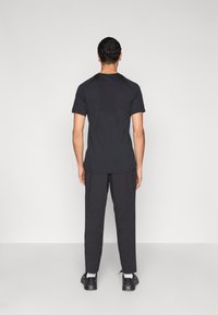 Μαύρο κοντομάνικο μπλουζάκι με λεία υφή, διακοσμημένο με διακριτικό ραφικό σχέδιο, συνδυασμένο με μαύρο παντελόνι στενής γραμμής και μαύρα παπούτσια.