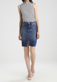 Denim kokerrok met een voorkniplijfje, vervaagde blauwe kleur, rafelige zoom, gecombineerd met een zwart-wit gestreept mouwloos topje. Roze heels.