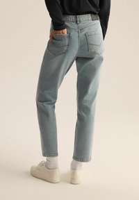 Jasnoniebieskie dżinsy o luźnym kroju, z tylkimi kieszeniami i kontrastowym wykończeniem, w połączeniu z białymi trampkami i skarpetkami.