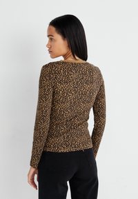 Smeđi dugi rukav majica s crnim uzorkom leopard, okruglim izrezom i prilagođenim dizajnom, uparena s crnim hlačama.