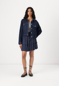 Denimjakke med knappeåpning, to brystlommer og cropped design. Kombinert med et navy polka prikket skjørt og svarte snøresko.