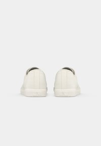 Hvite kanvas sneakers med gummisåle. Rund form, minimalistisk design, og diskret merking på hælen. Glatt tekstur med sømdetaljer.