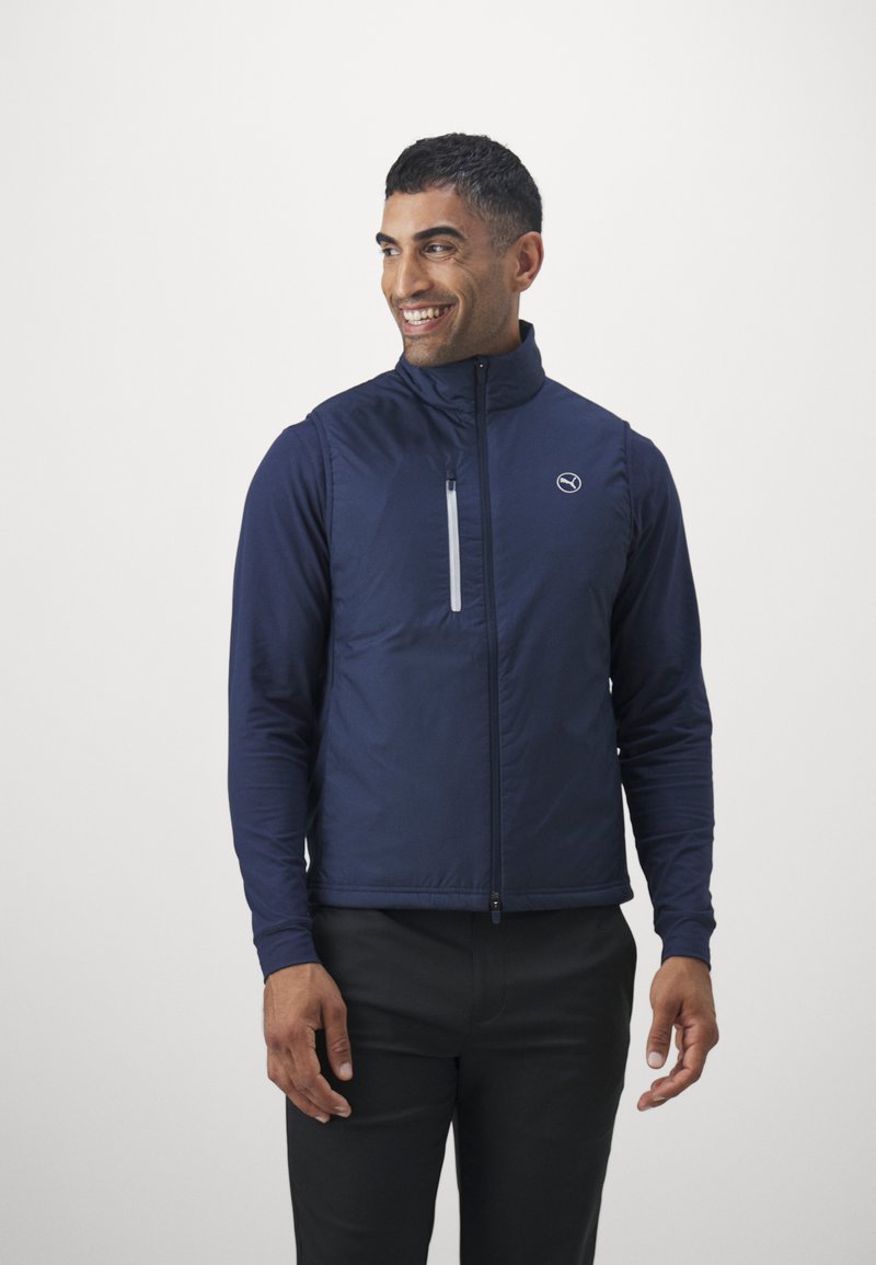 Gilet della marina con colletto alto, chiusura lampo frontale e dettagli riflettenti. Realizzato in materiale leggero, presenta un logo sul petto.
