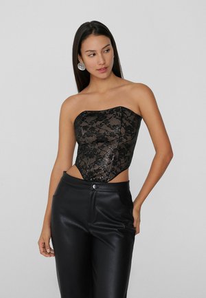 Bodysuit negro sin tirantes con superposición de encaje y acentos de lentejuelas, que presenta un diseño ajustado y lados descubiertos, combinado con pantalones de cuero de tiro alto.