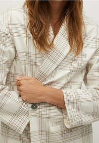 Blazer à carreaux crème avec des lignes marron et beige ; design croisé, revers à encoche et fermeture à un bouton. Tissu texturé.