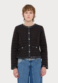 Svart quilted jakke med rund hals, frontlommer, detaljer i sølvknapper og sorte skinnakenter, sammen med lyseblå jeans.