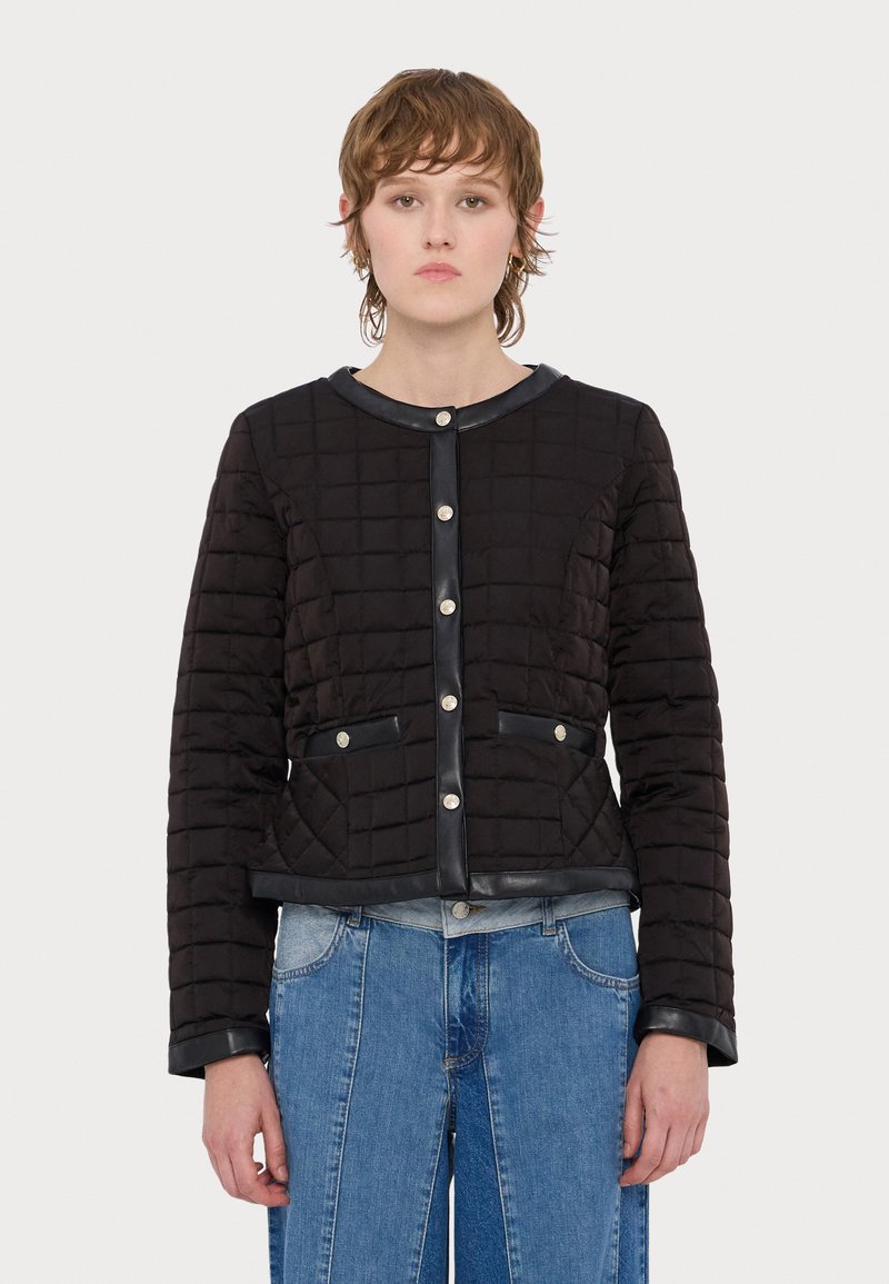 Svart quilted jakke med rund hals, frontlommer, detaljer i sølvknapper og sorte skinnakenter, sammen med lyseblå jeans.