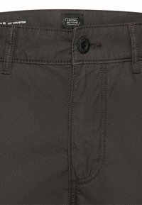 Mørkegrå teksturerede bukser med knaplukning, bæltestropper og Camel Active-mærkat på indersiden af linningen.