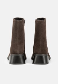 Brune suède ankelstøvler med en glat tekstur, skrå hæle og sidelukninger, med et rent, minimalistisk design.
