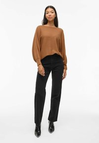 Pull ample côtelé marron avec manches longues, associé à un jean noir à jambe droite et des bottines noires. Design simple et texturé.