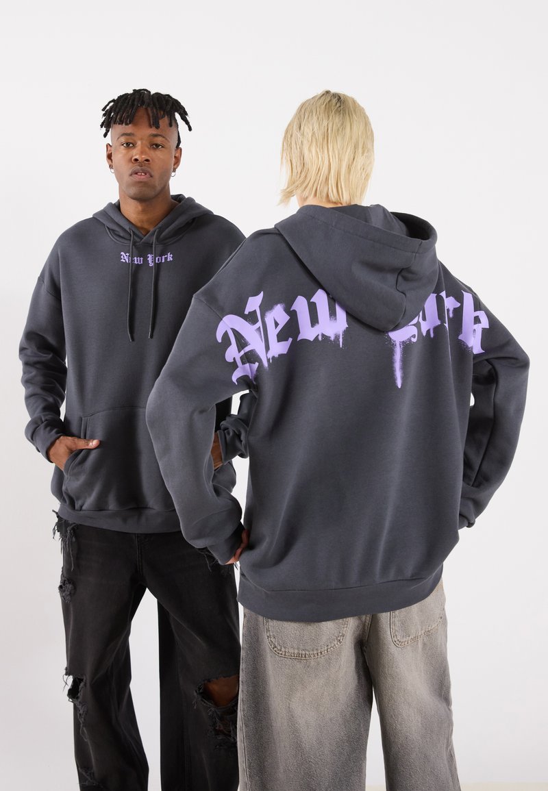Gray hoodie featuring "New York" in purple graffiti-style font on the back and front. Made of soft material with a kangaroo pocket.