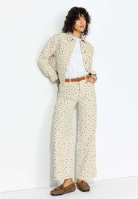 Chemise à imprimé floral beige et pantalon large assorti en tissu léger. Ceinture marron et chaussures à imprimé léopard marron.