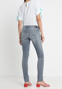 Blusa a rayas azul claro con mangas hasta el codo y detalles de lazo, combinada con jeans gris ajustados y sandalias de tacón bloque rosa.