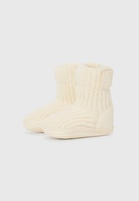 Bottines pour tout-petits couleur crème en matériau tricot doux avec une texture côtelée, présentant un bout arrondi et une semelle lisse semblable à du cuir.
