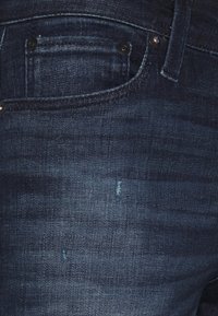 Denimjeans i mörkblått, med en slät textur, en liten framficka och subtila sömnadsdetaljer samt en svagt sliten effekt.