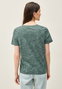 Kortærmet, grøn bluse med et bølget, tekstureret mønster. Blødt stof med afslappet pasform og rund halsudskæring, bæres med lyseblå jeans.