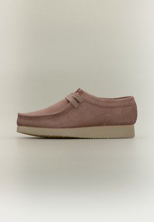 Chaussure slip-on en daim marron avec une semelle en caoutchouc beige, couture style mocassin et détail boucle sur le dessus.