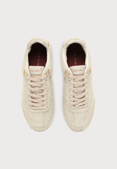 Paire de baskets en daim beige avec lacets beige, étiquettes de languette de marque et semelles intérieures foncées visibles de dessus.