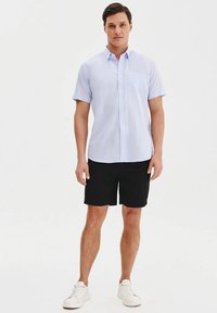 Jasnoniebieska koszula z krótkim rękawem zapinana na guziki, z kieszonką na piersi, w połączeniu z czarnymi szortami i białymi trampkami. Prosty design i swobodny krój.