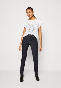 Hvit bomull T-skjorte med svart grafikk av himmelsk design, sammen med mørkeblå skinny jeans og svarte ankelstøvler.