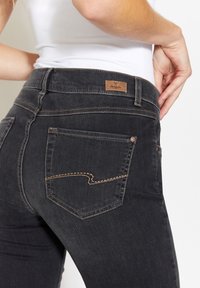 Jeans in denim nero con un design aderente, caratterizzati da un'etichetta in pelle marrone in vita e cuciture a contrasto sulle tasche posteriori.