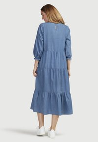 Sininen farkku mekko, jossa on kolmanneksen puhvihihat, kerroksellinen röyhelöhelma, avainaukko takaosassa ja rento malli. Yhdistetty valkoisiin lenkkareihin.