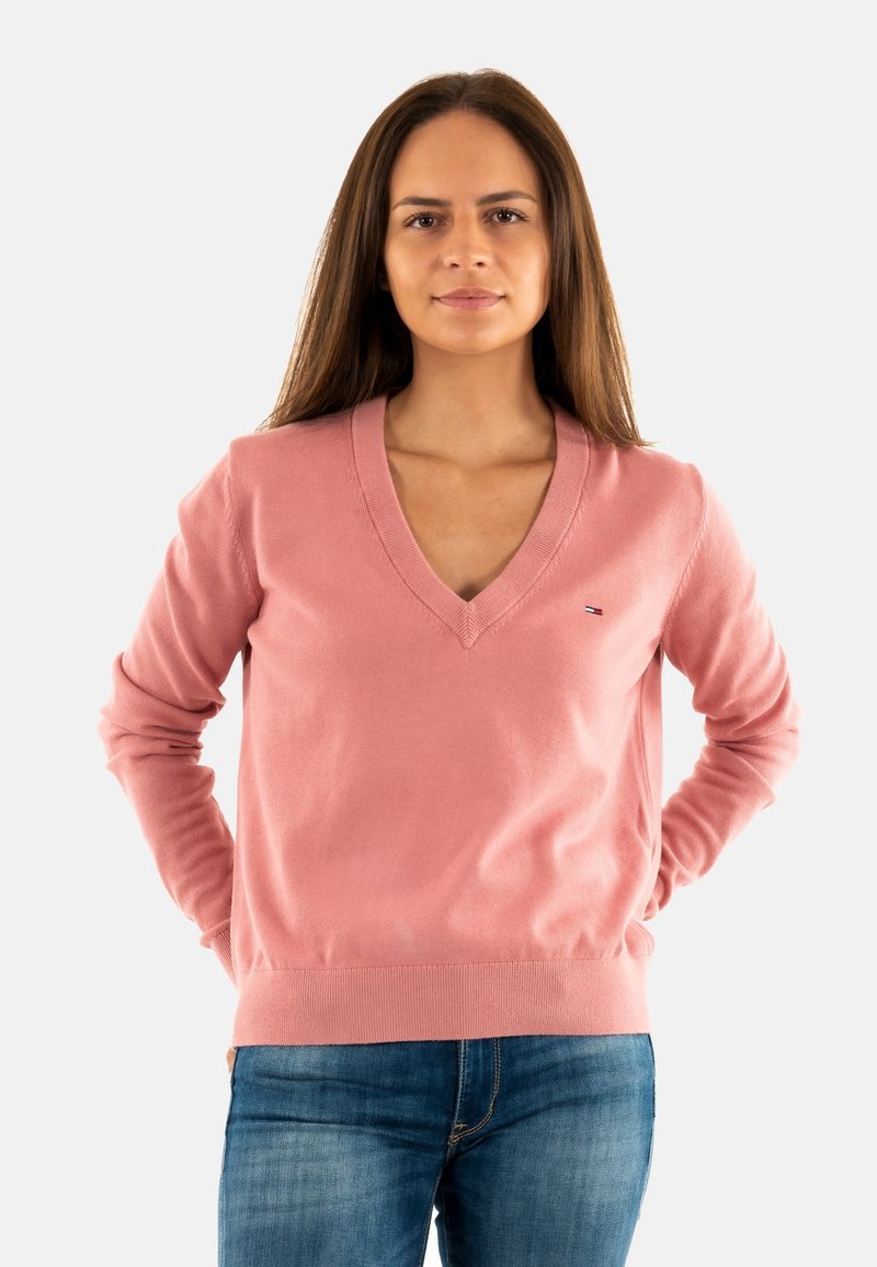 Maglione rosa chiaro a V realizzato in morbido tessuto, con maniche lunghe e orlo a costine. Piccolo logo sul petto.