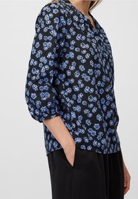 Blusa nera a fiori con fiori blu, maniche puff a 3/4 e scollatura a V. Tessuto leggero con vestibilità rilassata e tasca visibile.