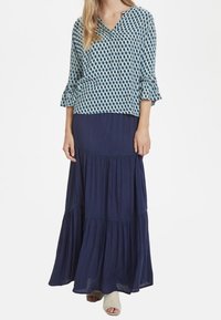 Top bluette a motivo con maniche a tre quarti con volant, abbinato a una gonna maxi blu navy a balze. Tessuto leggero, vestibilità rilassata e dettagli di design sottili.