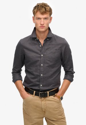 Donkergrijze button-up overhemd met een kraag, subtiele textuur en een borstzak, gecombineerd met kaki broek en een zwarte riem.