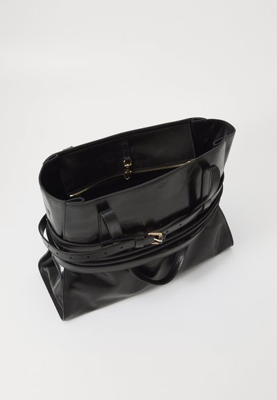 Black leather tote bag with a structured design. Features top handles, a removable shoulder strap, and a zippered compartment. Smooth texture.