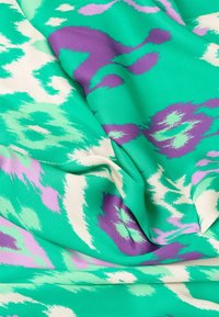 Tkanina w wzory z odcieniami zieleni, lawendy i kremu. Gładka faktura z abstrakcyjnym, falistym wzorem.