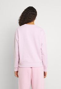 Sweatshirt rose clair avec un col rond, des épaules tombantes et des poignets côtelés. Texture douce et coupe décontractée. Aucun logo ni motif visible.