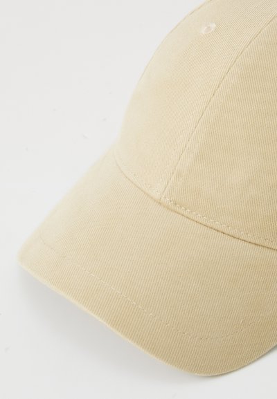 Beige cap made of ribbed fabric; features a rounded shape, a stitched brim, and a small vent on top. Smooth texture with visible stitching.
