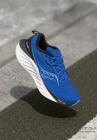 Scarpa da corsa blu con tomaia in mesh testurizzato, accenti neri, suola bianca ammortizzata e marchio Saucony visibile. Design leggero.