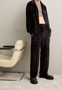 Zwarte velours trainingspak met een jas met rits en elastische taillebroek, gecombineerd met chunky bruine plateauzolen met studs.