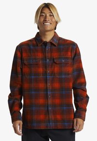 Rød og sort ternet flannel skjorte med blå detaljer, knaplukning foran, to brystlommer og lange ærmer med knappede manchetter.