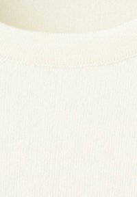 Detailní záběr na bílou žebrovanou pleteninu ukazující kulatý průkrčník a jemnou texturu.