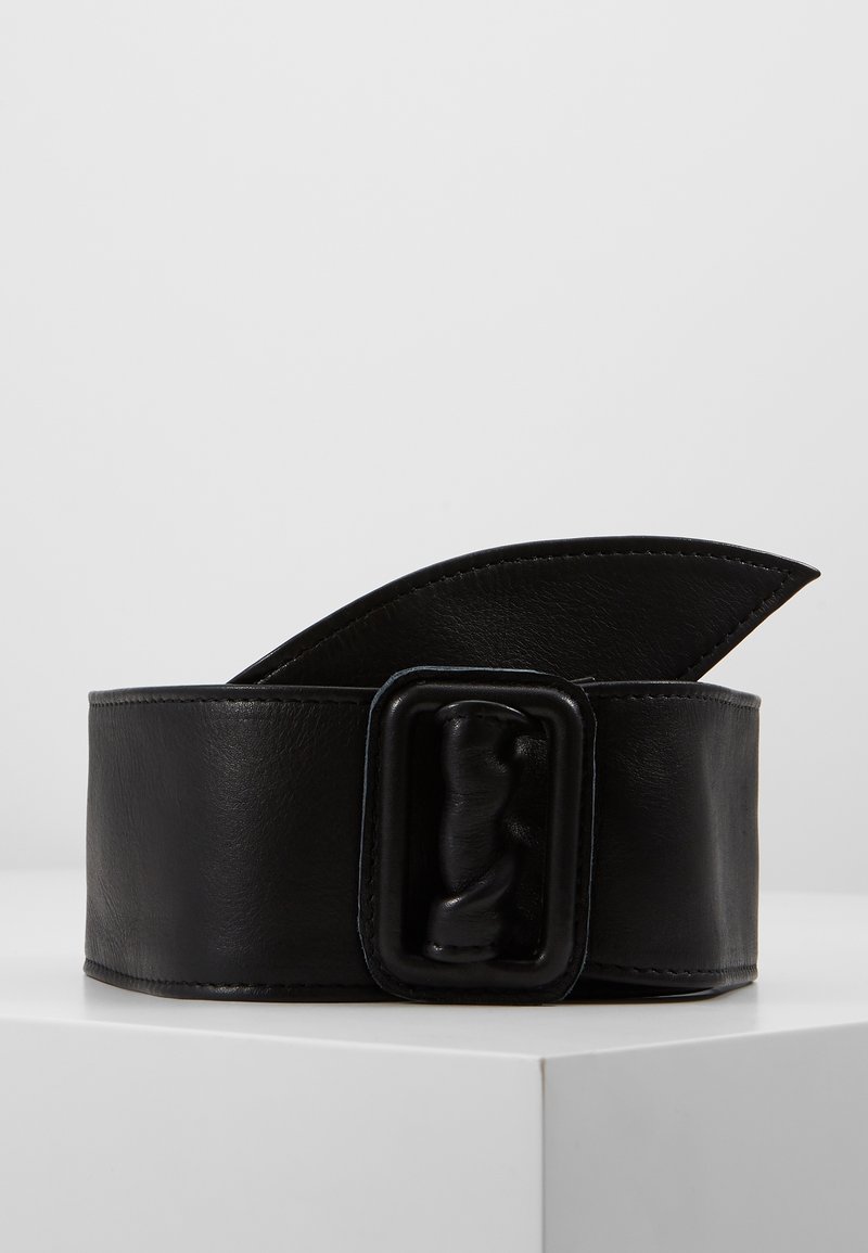 Ceinture large en cuir noir avec une grande boucle rectangulaire, présentée enroulée sur une surface blanche sur fond gris.