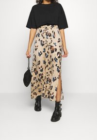 Maxi sukně v béžové barvě s pestrým leopardím potiskem. Obsahuje elastický pas, boční rozparky a splývavý, lehký materiál. Kombinováno s černým oversized tričkem a kotníkovými botami.