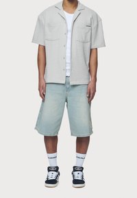 Kurzärmeliges graues Texturhemd mit zwei Fronttaschen, kombiniert mit hellblauen Denim-Shorts. Schwarze Sneakers mit weißen Akzenten vervollständigen das Outfit.