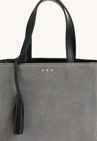 Sac fourre-tout en suédine grise avec poignées en cuir noir et détail de pompon, agrémenté de trois petites rivets dorés au centre avant.
