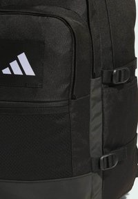 Schwarzer Rucksack mit strukturierter Oberfläche, der ein einfarbiges Paneel und Netzdetails aufweist. Verfügt über verstellbare Gurte und ein weißes Logo-Akzent.