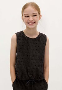 Zwarte mouwloze top met geborduurde driehoekige patronen en kleine uitsneden. Heeft een ronde halslijn en een geraffineerde taille met een drawstring.