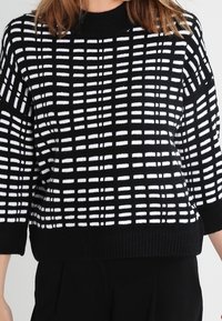 Czarnobiały sweter dziany w kratę z szerokimi rękawami i prążkowanym dołem. Projekt jest casualowy i teksturowany.
