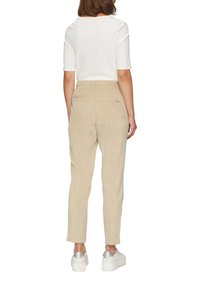 Beige kordfluweelbyxor med rak ben, med bakfickor och en subtil logodetalj. Stylingen kompletteras med en vit ribbad t-shirt med kort ärm och sneakers.