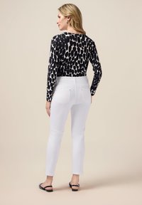 Långärmad topp med svart och vit abstrakt mönster; kombinerad med vita jeans. Modellen bär platta skor; vy från baksidan.