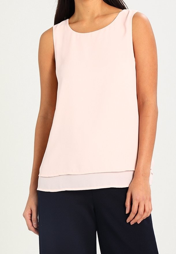 Blouse sans manches rose en tissu léger avec un col dégagé et un ourlet à plusieurs couches, assortie à un pantalon bleu marine. Texture lisse.